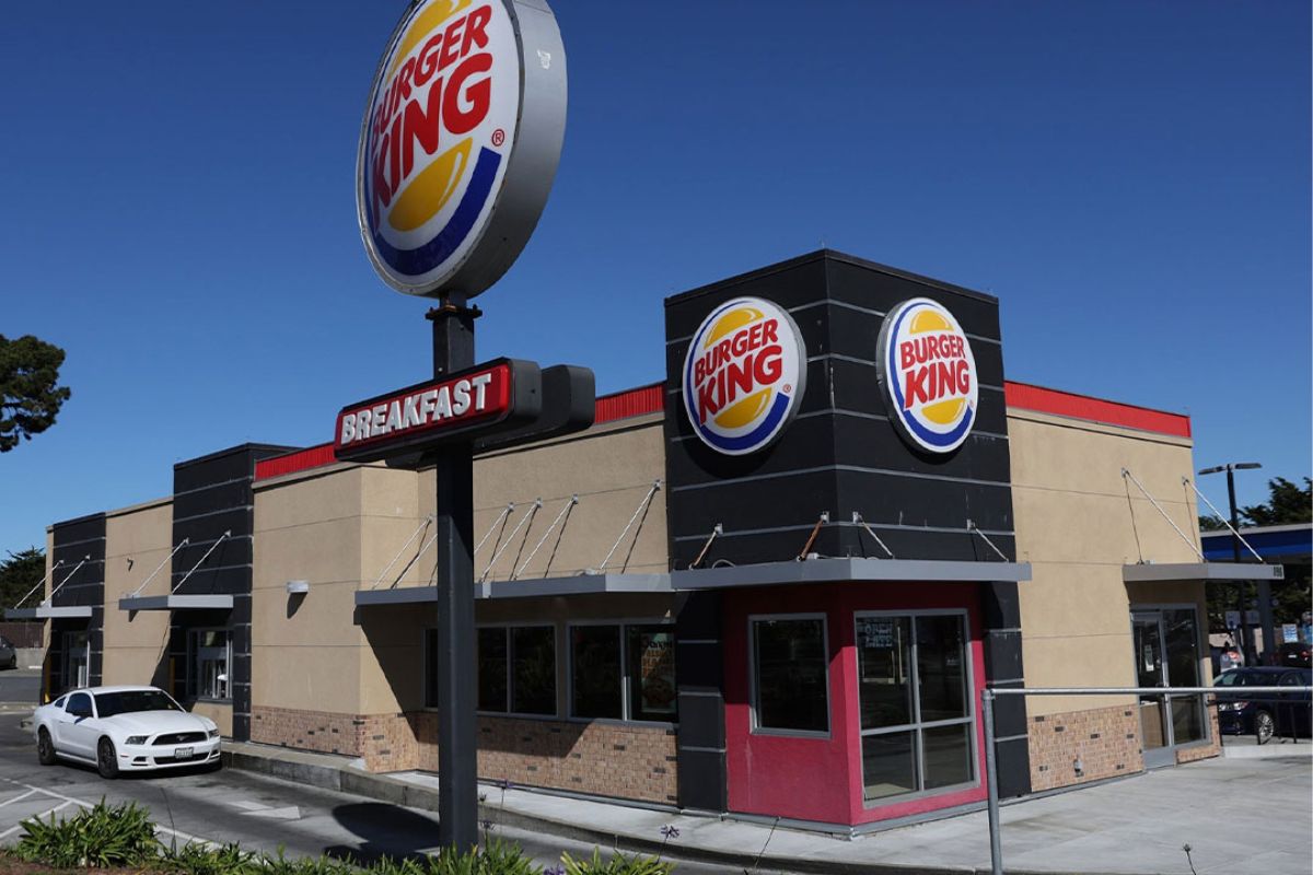 Un hombre usando un delantal entregando una hamburguesa envuelta a una mujer en un puesto de comida