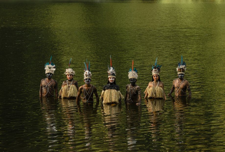 Tribal members in traditional attire stand in water, Tingo María, Peru.