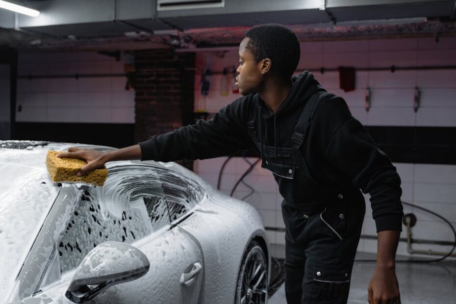 A person washing a car with a sponge, deep cleaning in a garage setting.