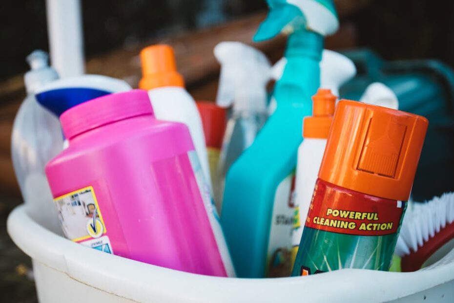 Close-up of assorted cleaning supplies in a bucket outdoors, showcasing various detergents and sprays.