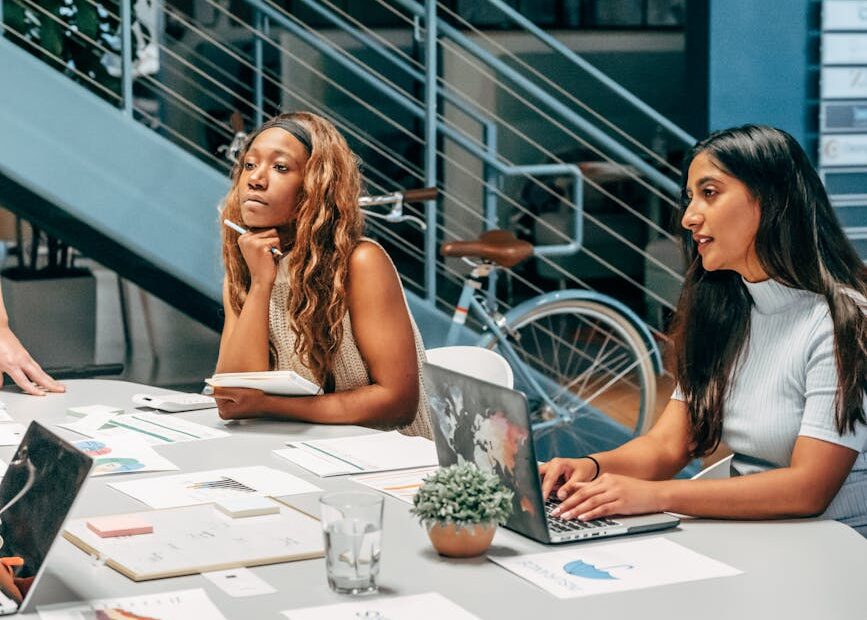 Diverse women engaging in a collaborative meeting at an office desk, focused on planning and innovation.