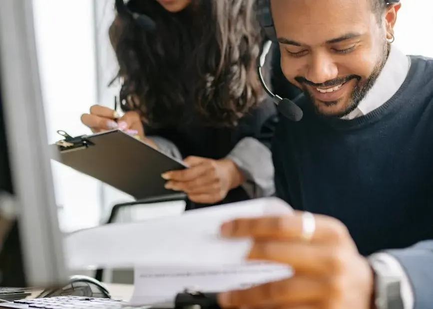 Two diverse call center employees collaborating with documents and headsets.