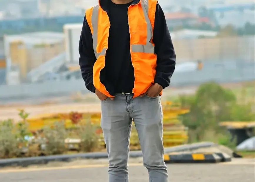 A construction worker stands confidently outdoors wearing safety gear and helmet.