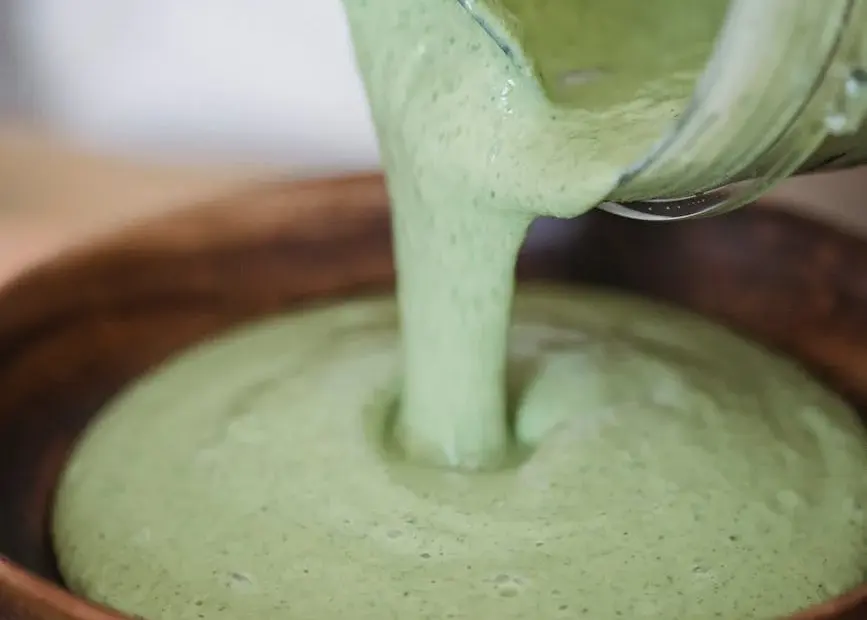 Close-up of creamy green smoothie being poured into a wooden bowl.