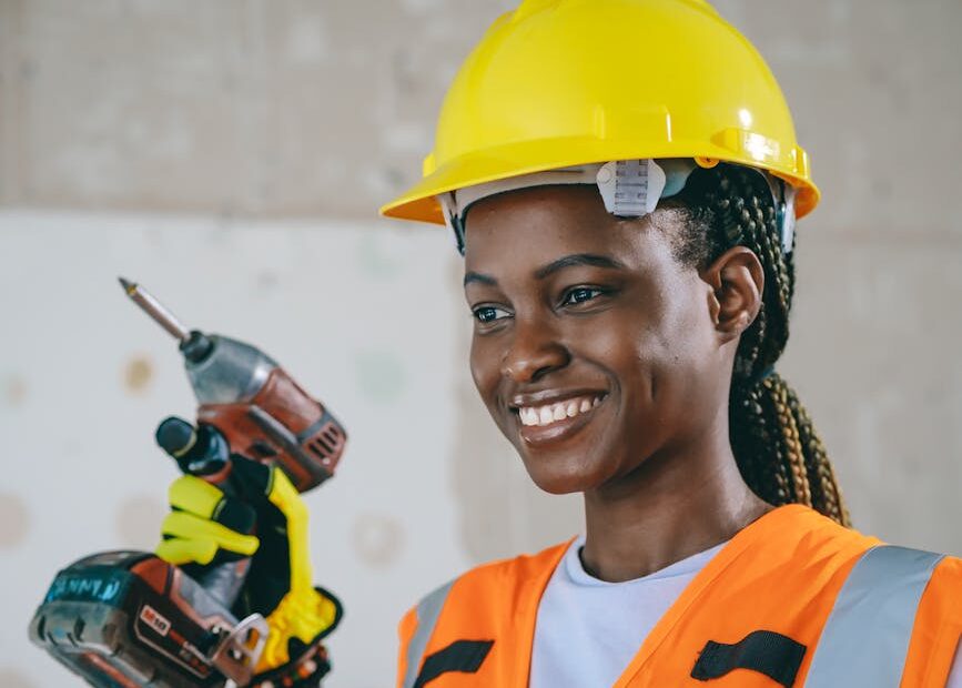 Confident female construction worker in safety gear smiling indoors.