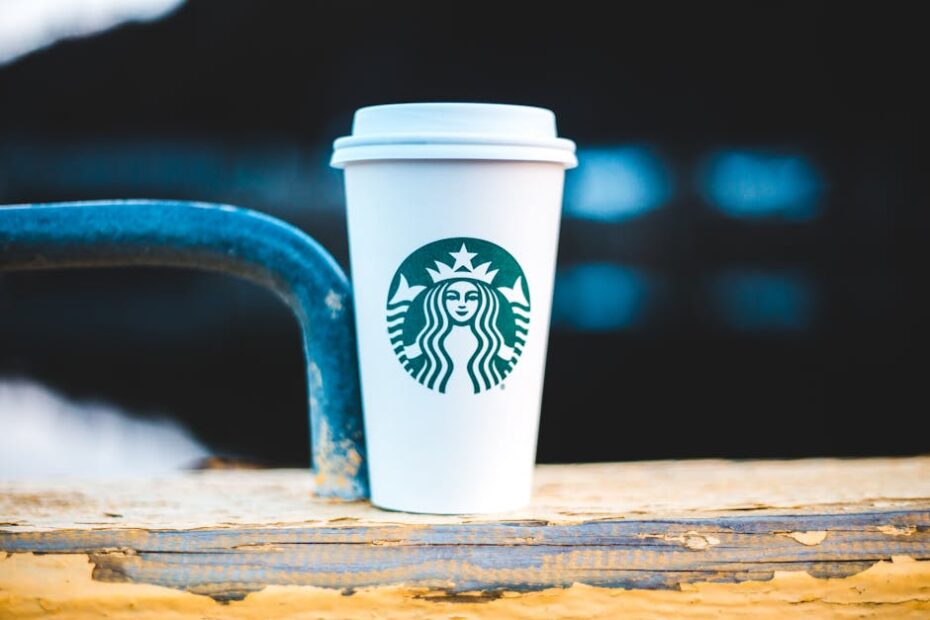 A white coffee cup with a logo on a rustic wooden rail, perfect for a cozy outdoor coffee moment.
