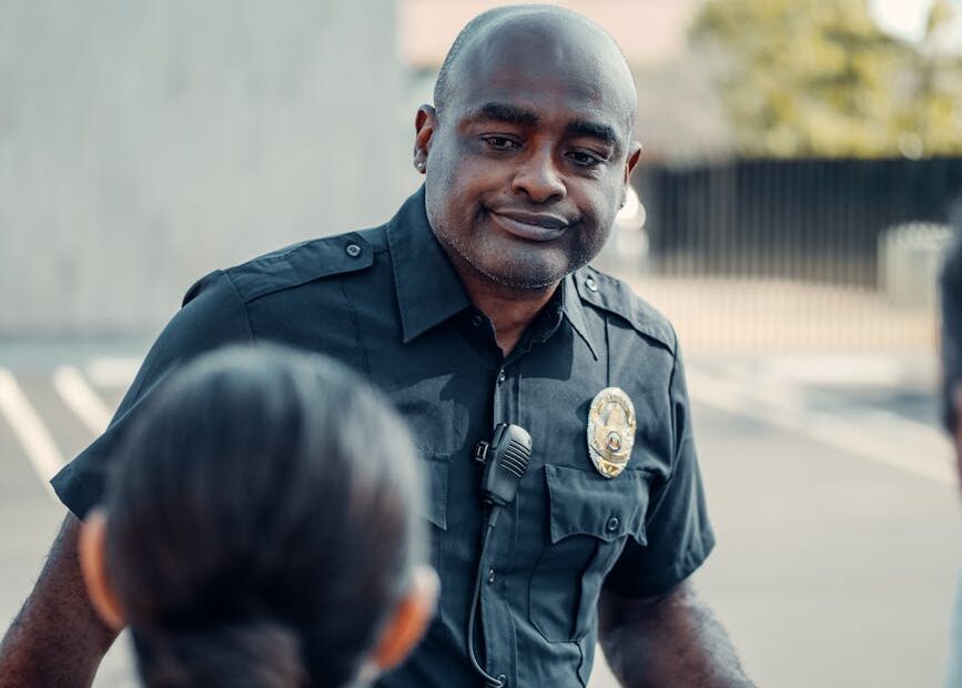 A police officer in uniform engaging warmly with people outdoors.