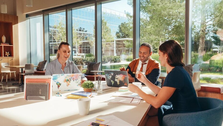 Three colleagues brainstorming with laptops in a well-lit office.